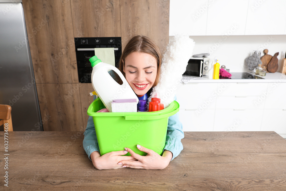 Young woman with cleaning supplies at table in kitchen