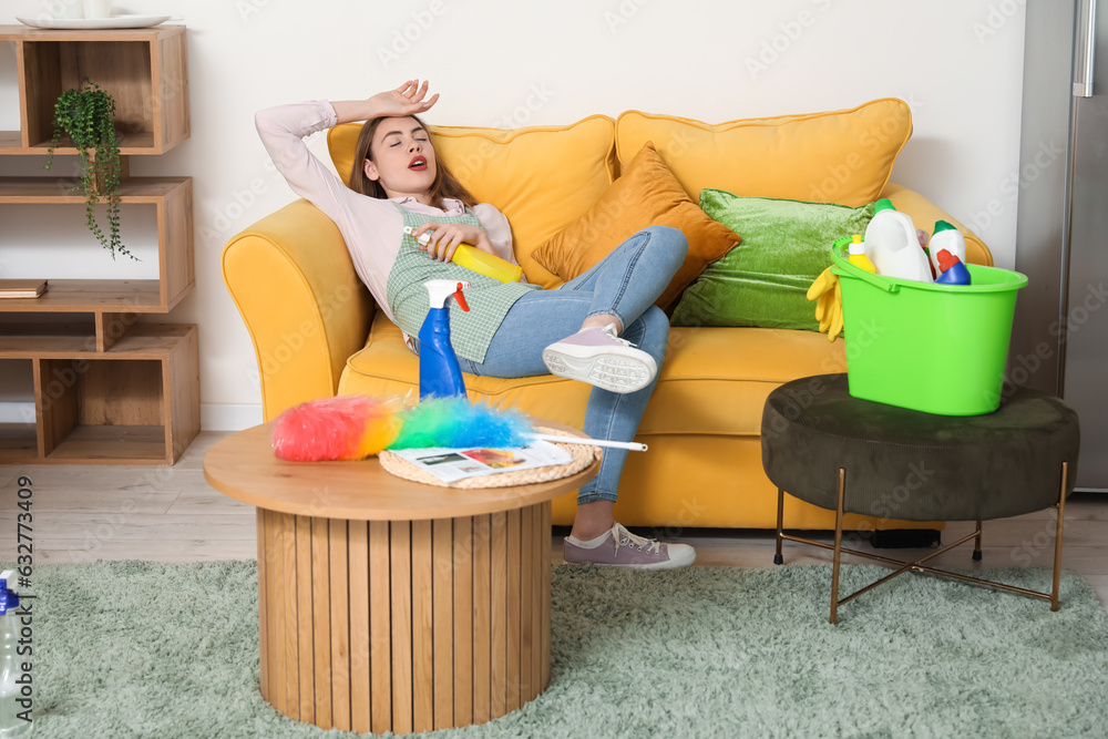 Tired young woman with bottle of detergent after cleaning at home