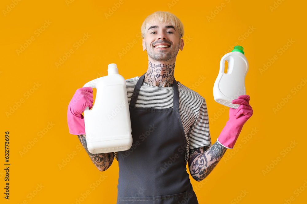 Young tattooed man with bottles of detergent on orange background