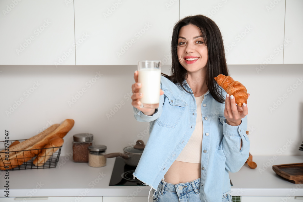 Beautiful woman with glass of milk and tasty croissant in kitchen