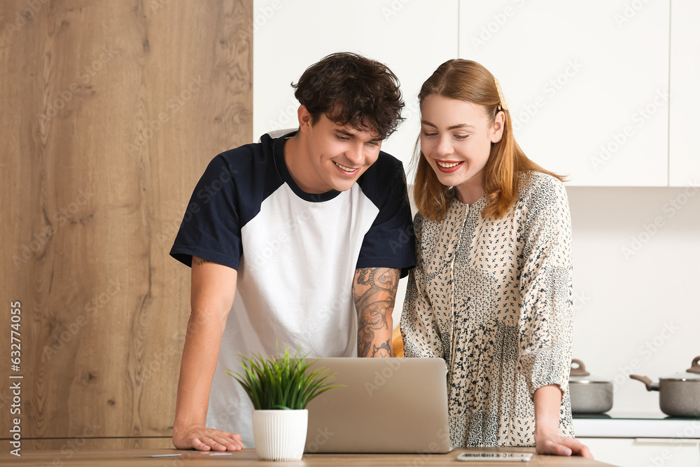 Young couple with laptop shopping online in kitchen