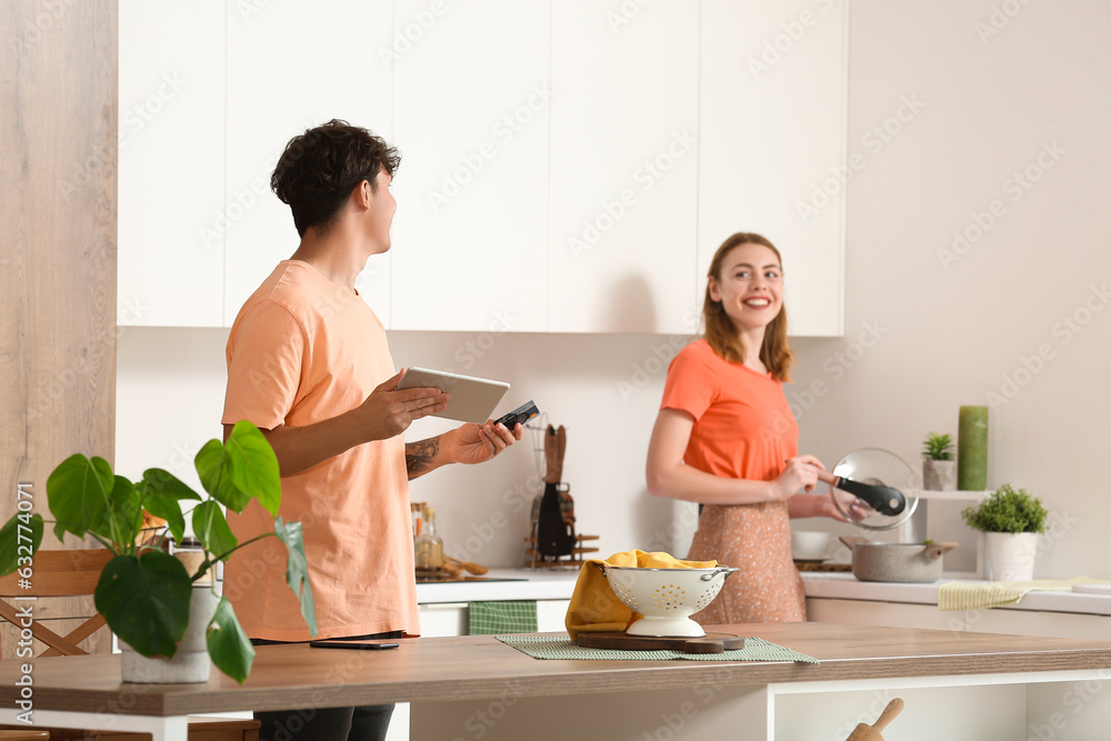 Young couple with tablet computer and gift card shopping online in kitchen