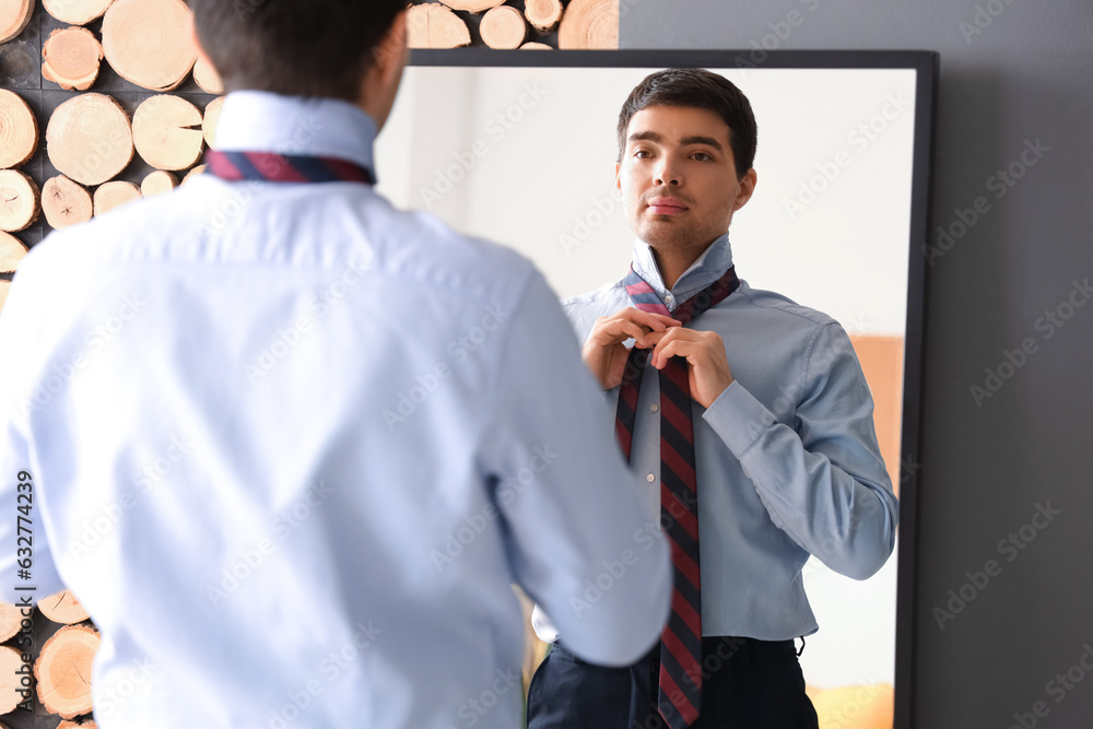 Young businessman tying his necktie in front of mirror at home