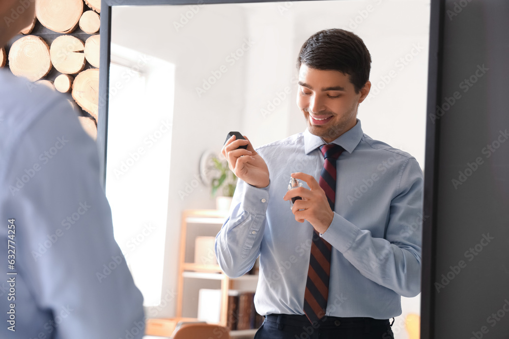 Young businessman applying perfume in front of mirror at home