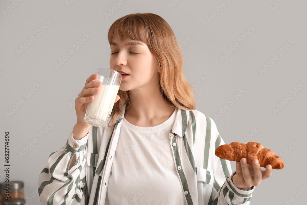 Young woman with croissant drinking milk in kitchen