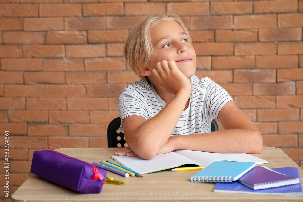 Little boy doing homework at table near brick wall