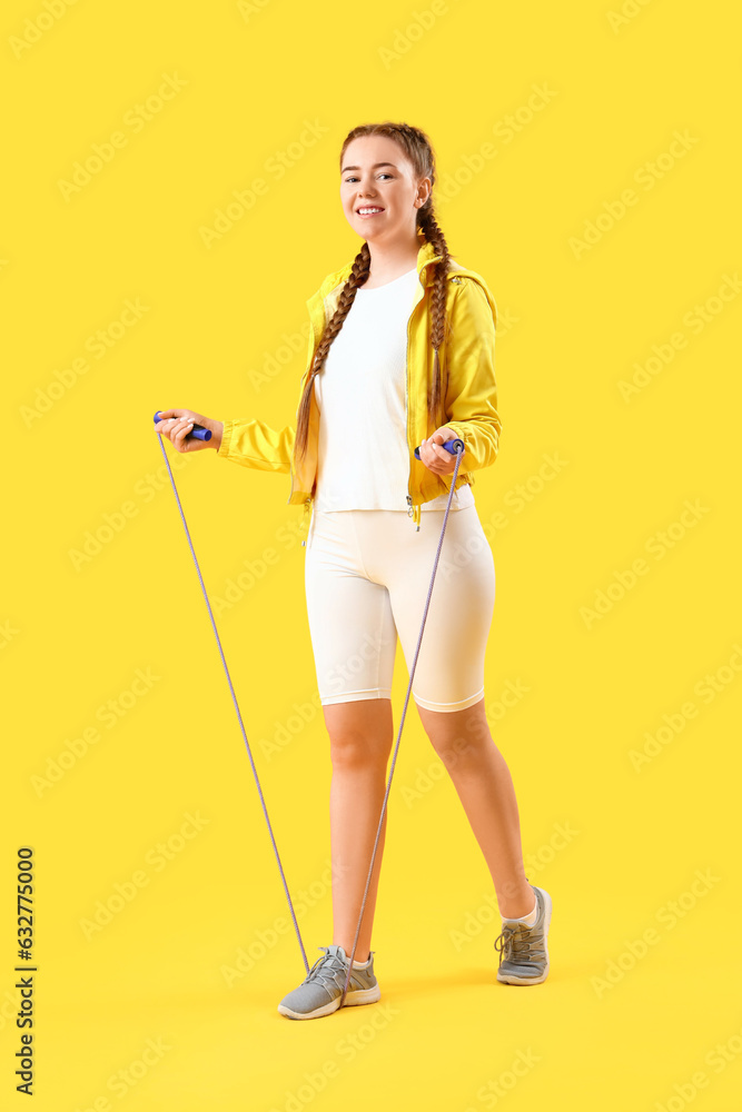 Sporty young woman with skipping rope on yellow background