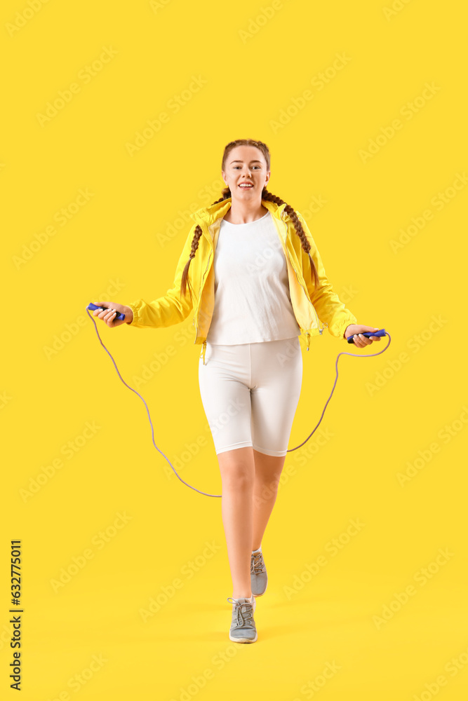 Sporty young woman jumping with rope on yellow background