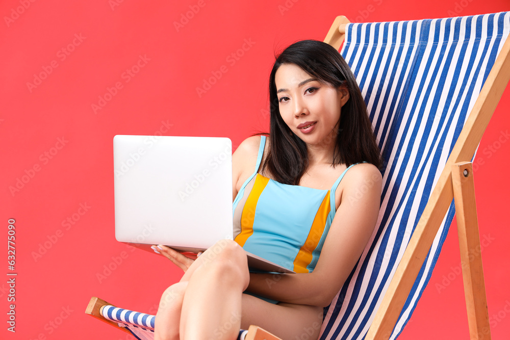 Beautiful Asian woman using laptop in deck chair on red background