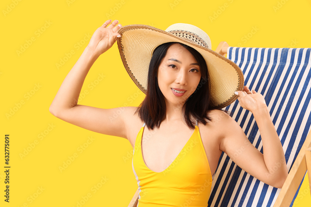 Beautiful Asian woman relaxing in deck chair on yellow background