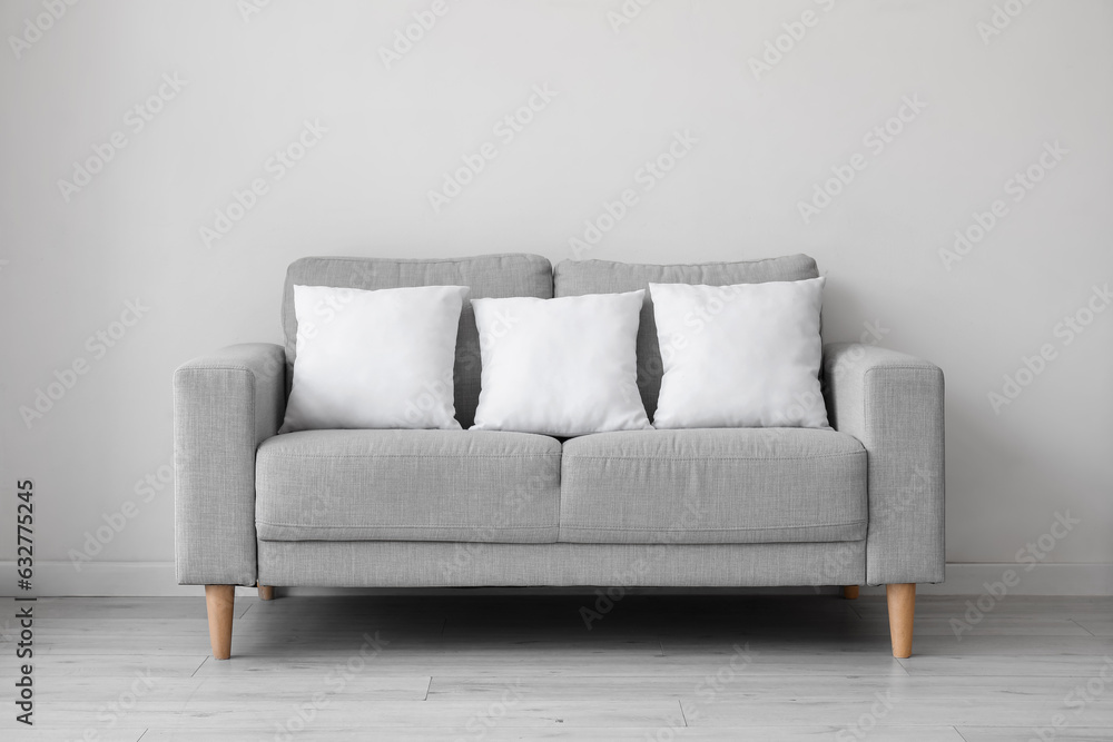 Grey sofa with pillows near white wall