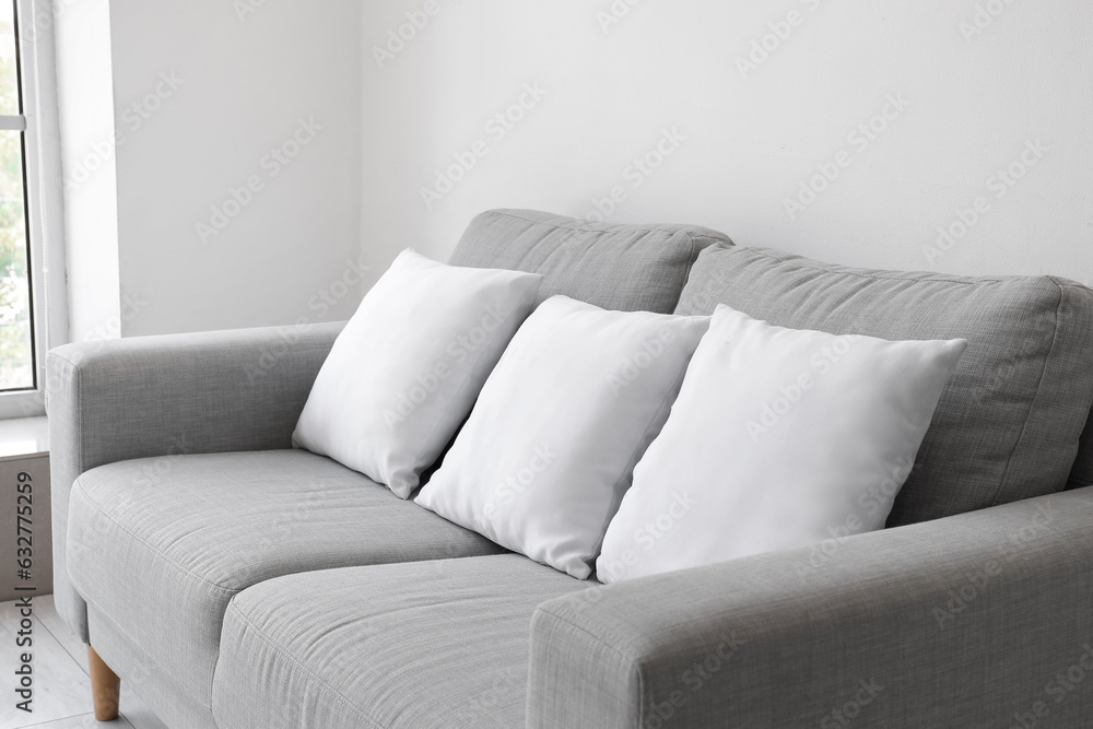 Grey sofa with pillows near white wall