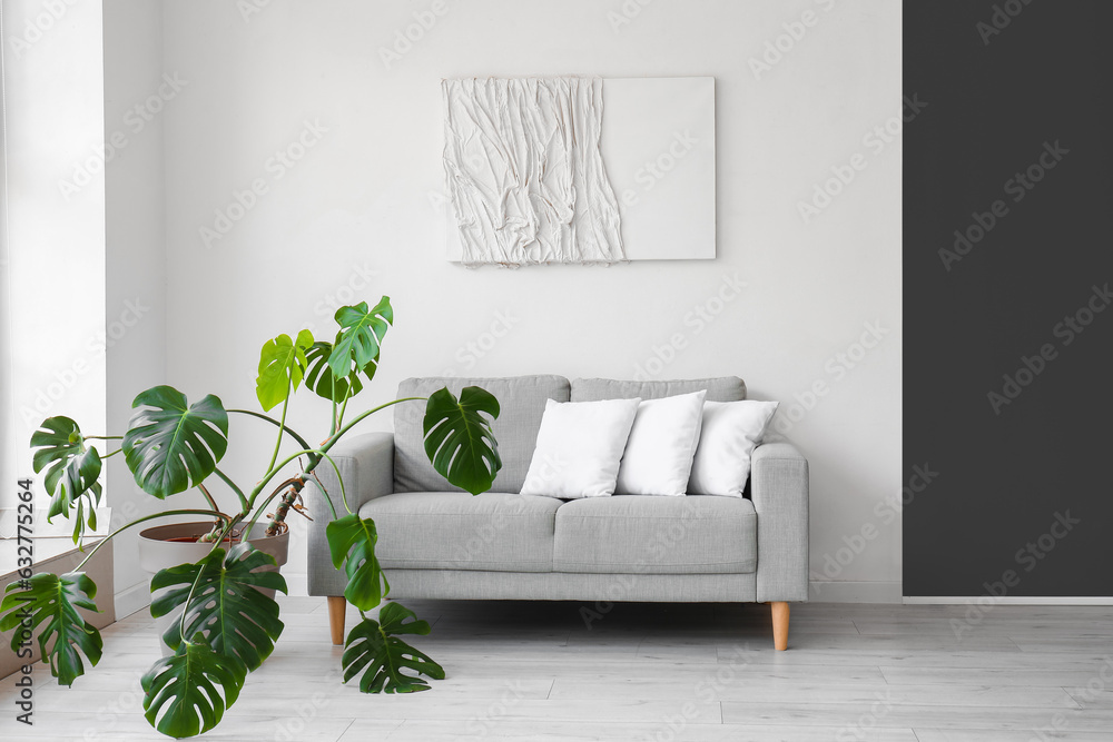 Grey sofa with pillows and houseplant near white wall