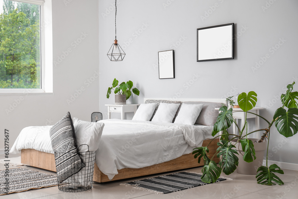 Interior of modern bedroom with comfortable double bed, white pillows and houseplants