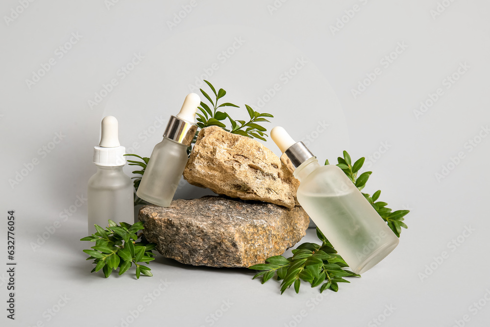 Composition with bottles of essential oil, stones and plant branches on light background