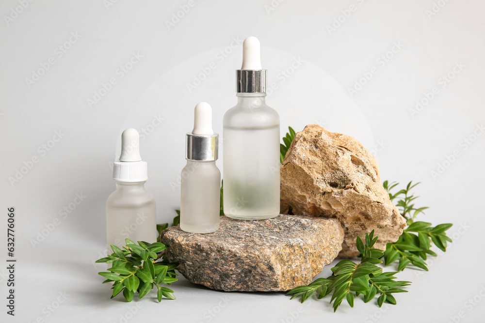 Composition with bottles of essential oil, stones and plant branches on light background