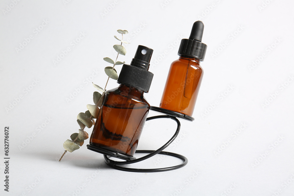 Bottles of cosmetic products and eucalyptus branch on light background