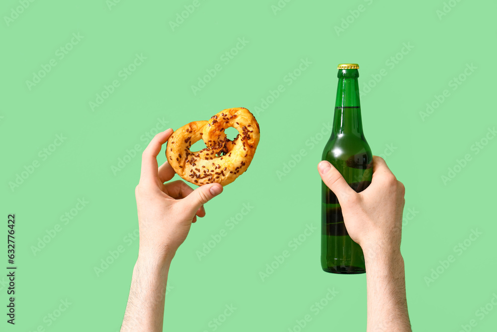 Man with bottle of beer and pretzel on green background