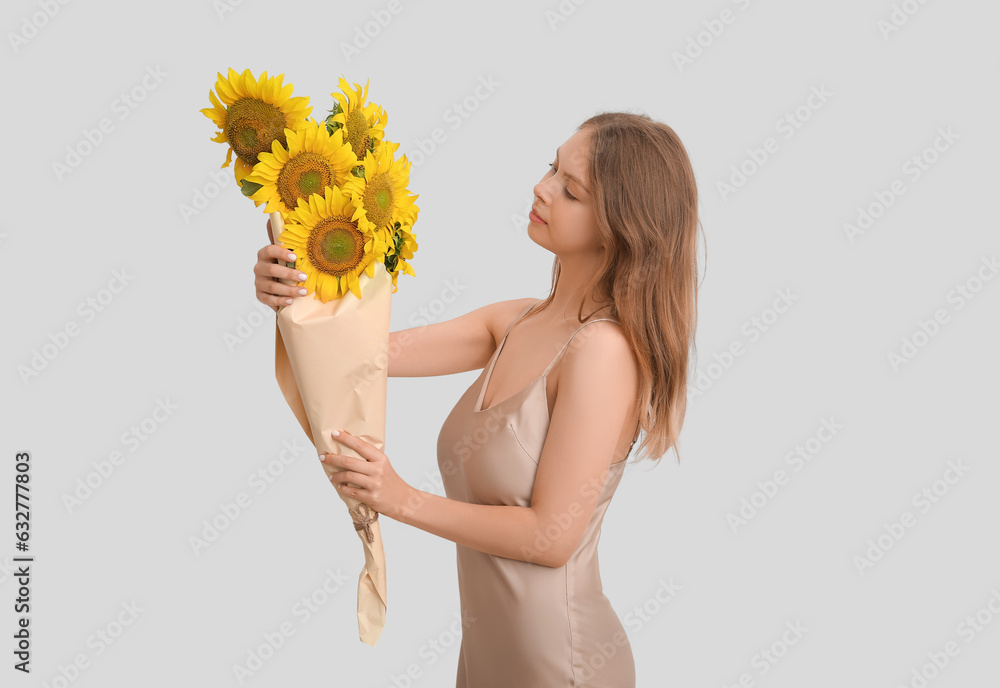 Young woman holding bouquet of beautiful sunflowers in paper on light background