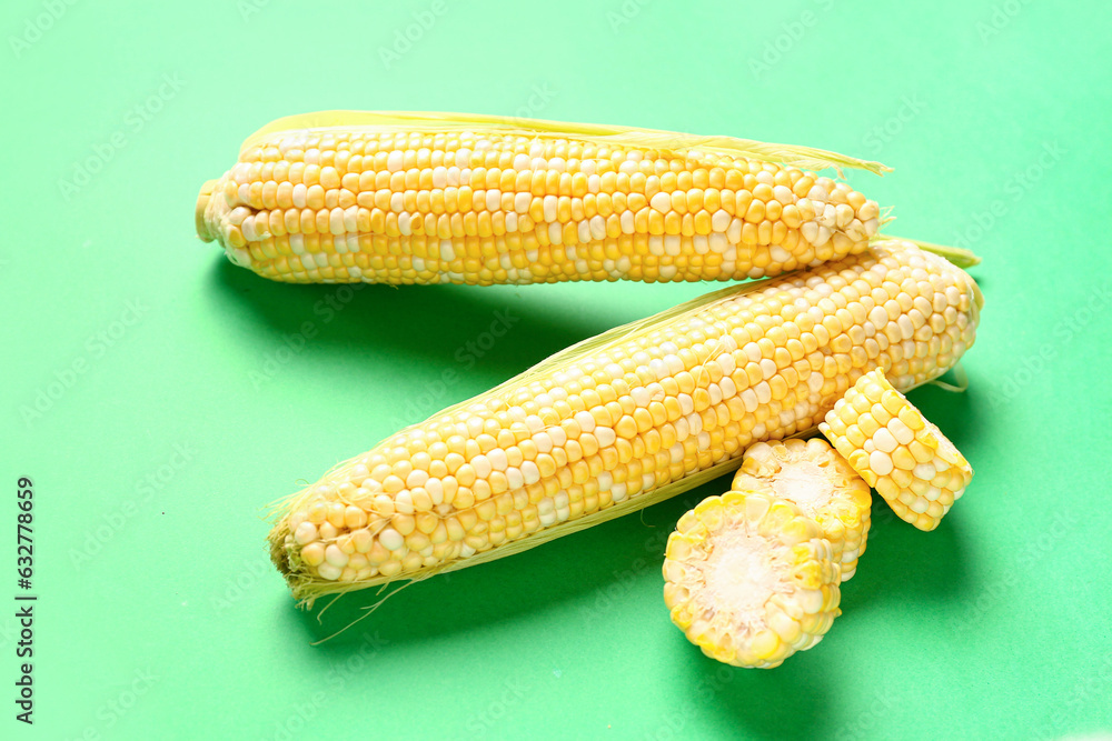 Fresh corn cobs on green background