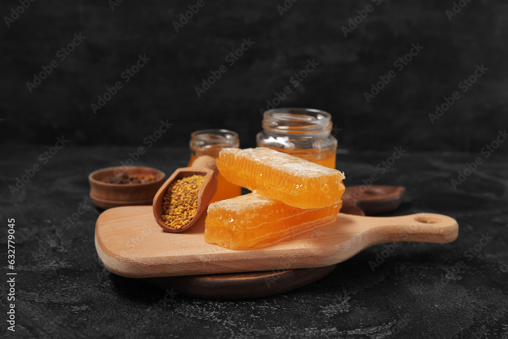 Wooden board with fresh honeycombs and bee pollen on dark background