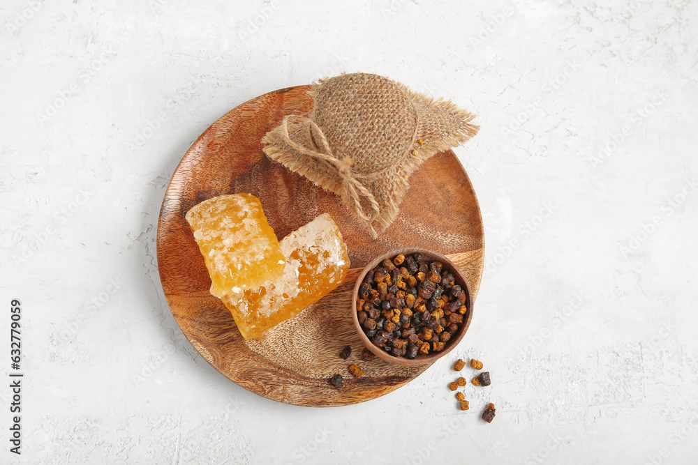 Wooden plate with honey, combs and beebread on light background