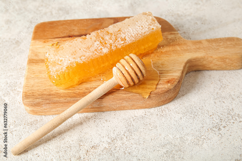 Wooden board with fresh honeycomb and dipper on light background