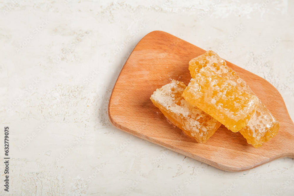 Wooden board with sweet honeycombs on light background