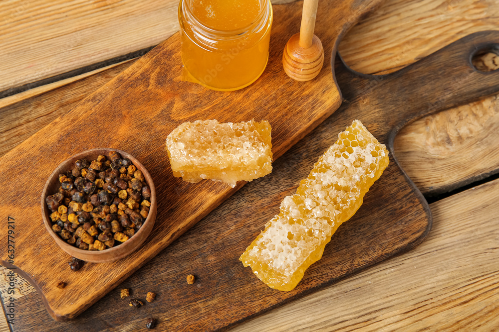 Kitchen board with sweet honey, combs and beebread on wooden background, closeup