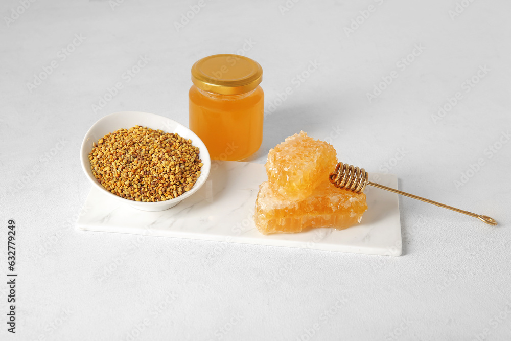 Board with bowl of bee pollen, honey and combs on light background