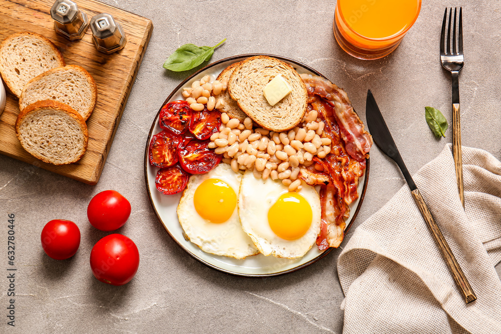 Plate with tasty English breakfast and glass of juice on grey background