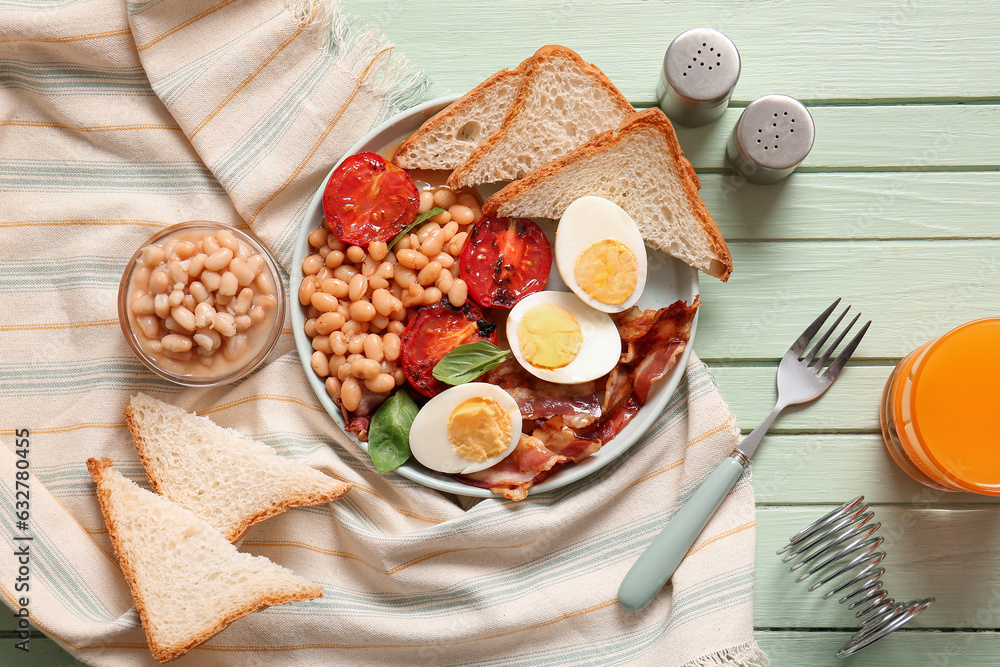 Plate with tasty English breakfast and glass of juice on green wooden background