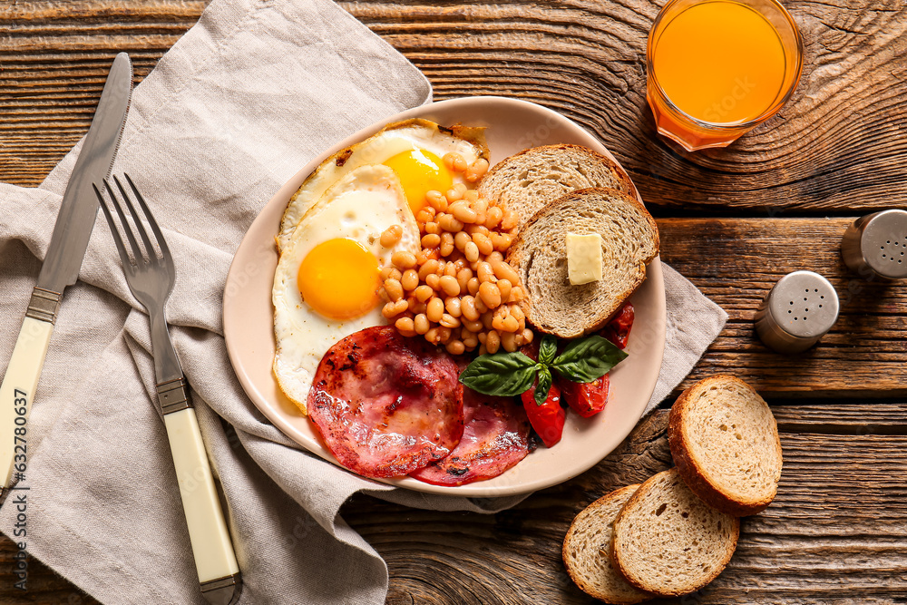 Plate with tasty English breakfast and glass of juice on wooden background