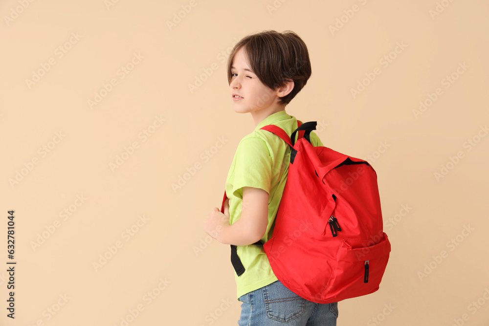 Little boy with backpack on beige background