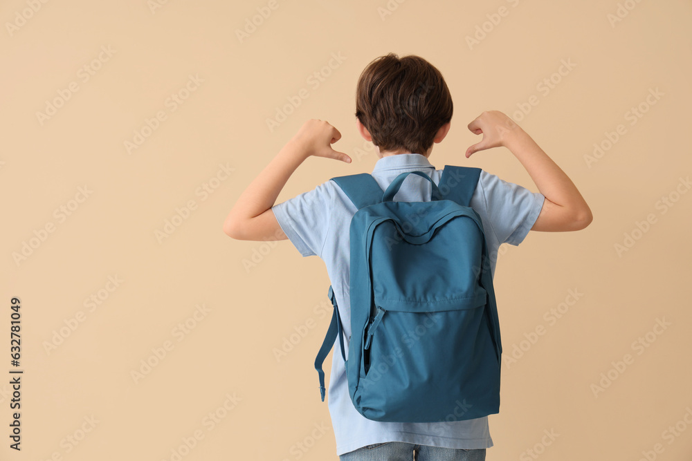 Little boy pointing at backpack on beige background, back view