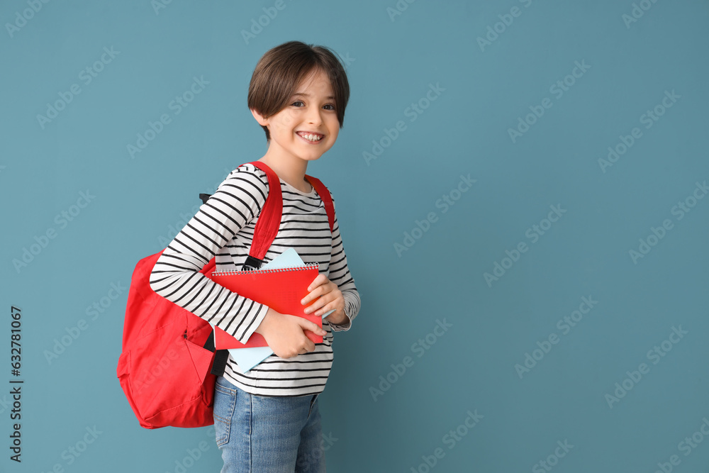 Happy little boy with backpack and notebooks on blue background