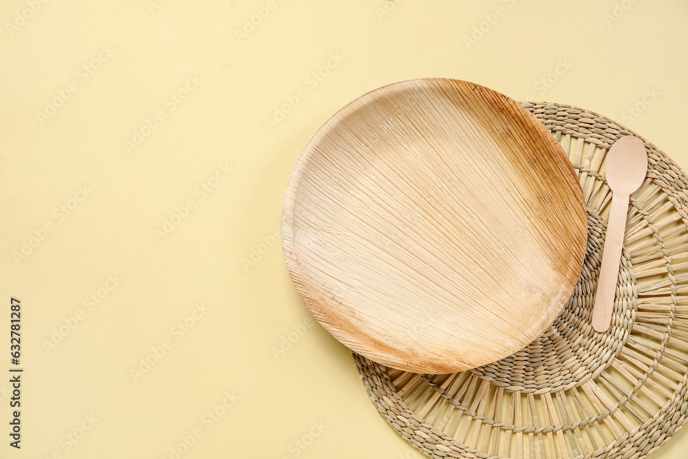 Wicker mat with wooden plate and spoon on beige background