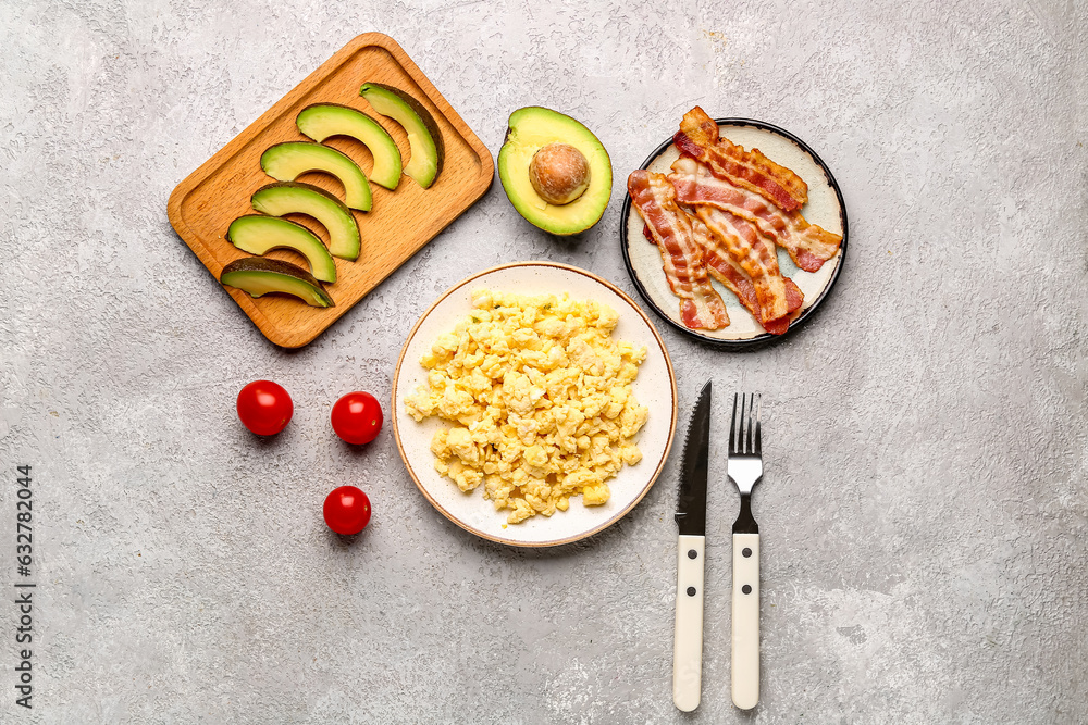 Plates of tasty scrambled eggs, bacon and avocado on grey background