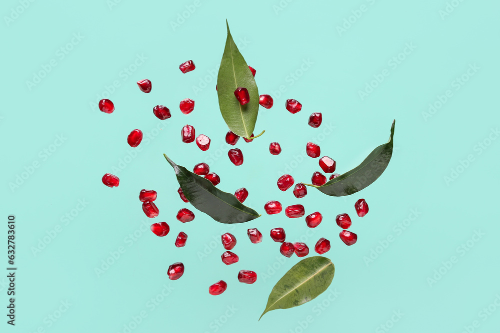 Flying fresh pomegranate seeds and leaves on turquoise background