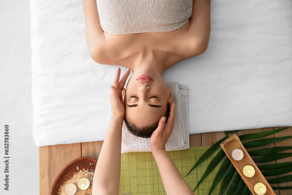 Pretty young woman having face massage in spa salon, top view