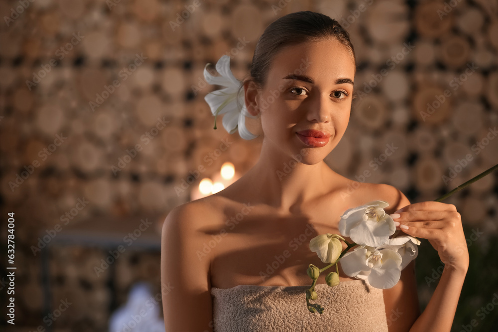 Pretty young woman with flowers in spa salon