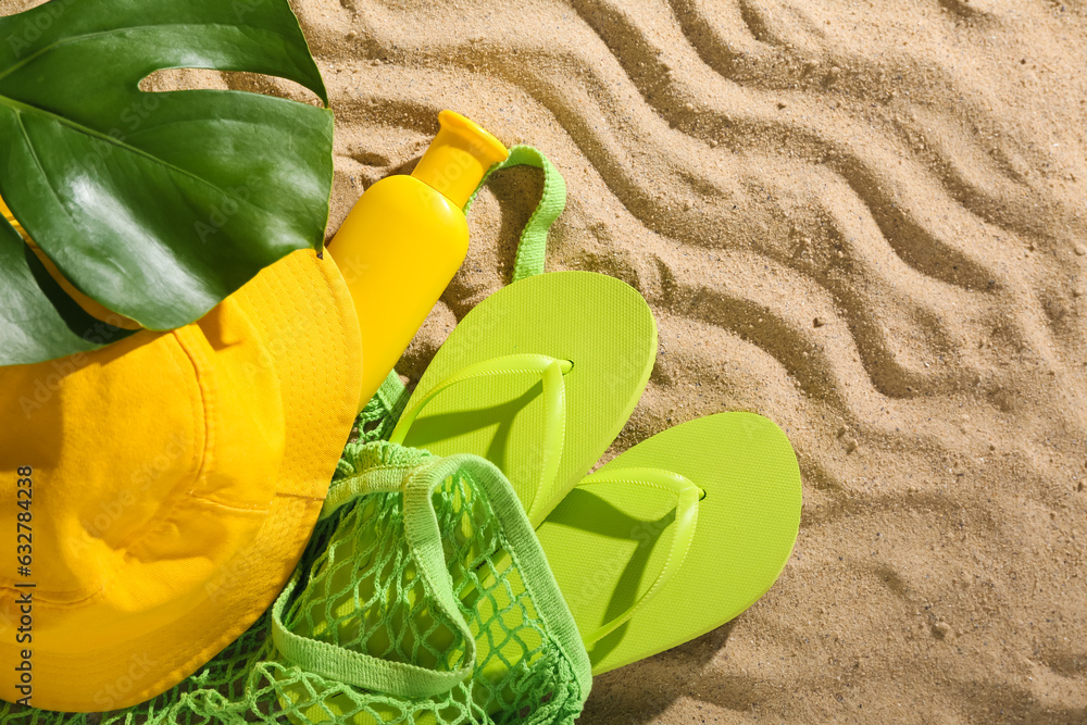 Pair of green flip flops with panama and wicker bag on sandy background