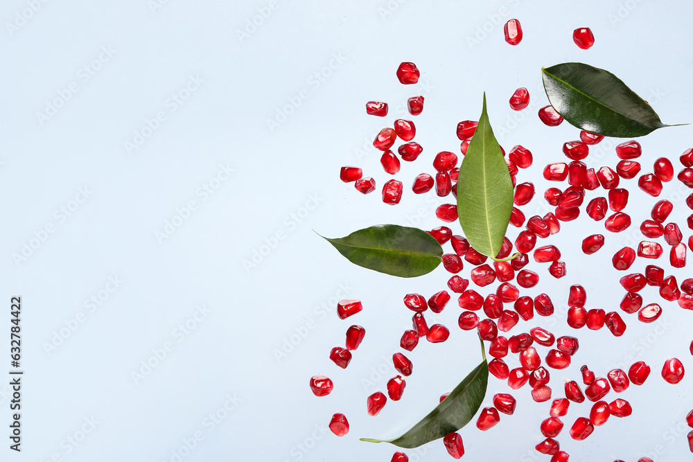 Flying fresh pomegranate seeds and leaves on blue background