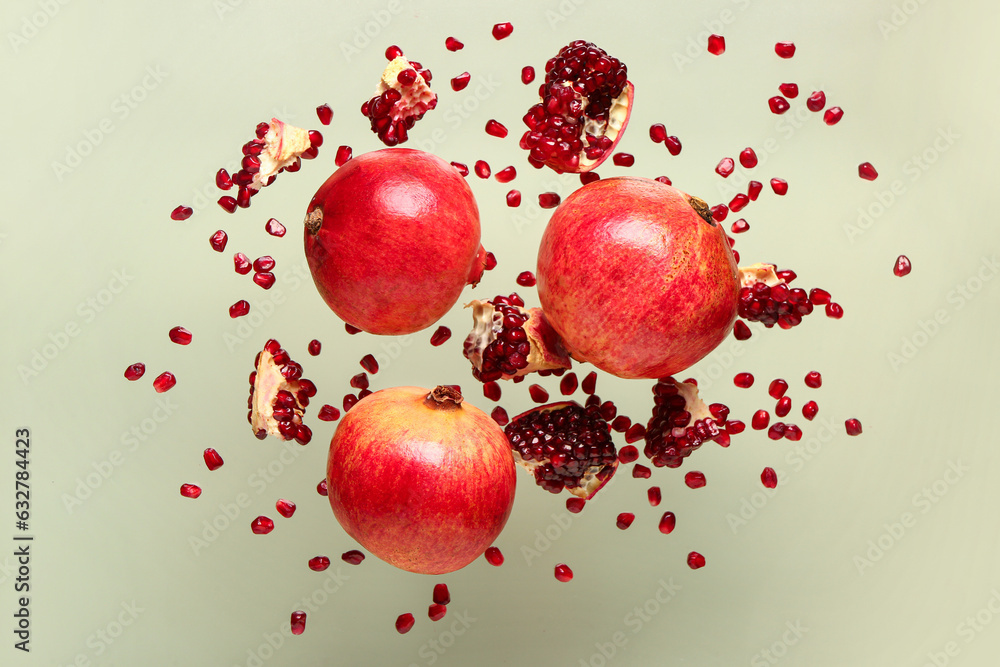 Flying fresh pomegranates with seeds on green background