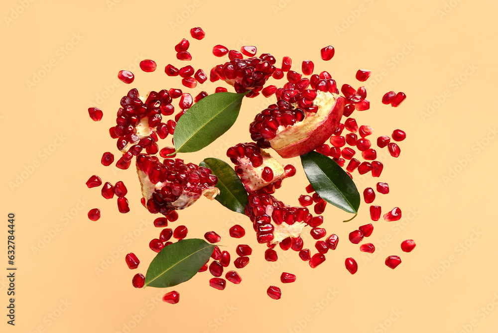 Flying fresh pomegranates with seeds and leaves on orange background