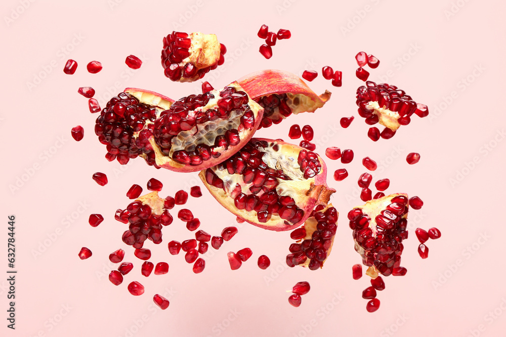 Flying fresh pomegranates with seeds on pink background