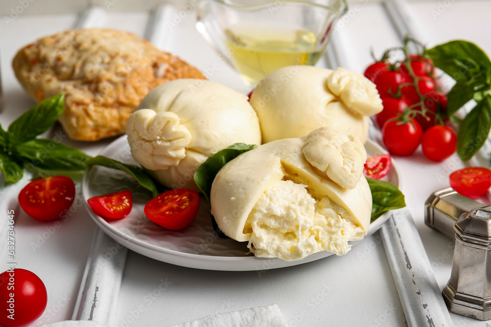 Plate of tasty Burrata cheese with basil and tomatoes on white background