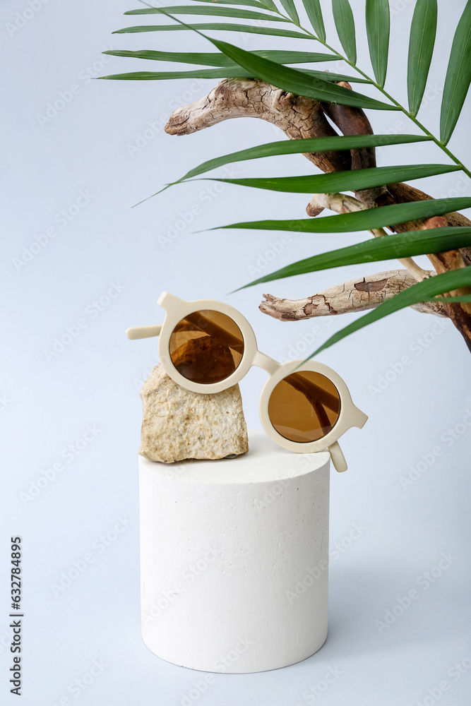 Decorative podium with stylish sunglasses and palm leaf on white background