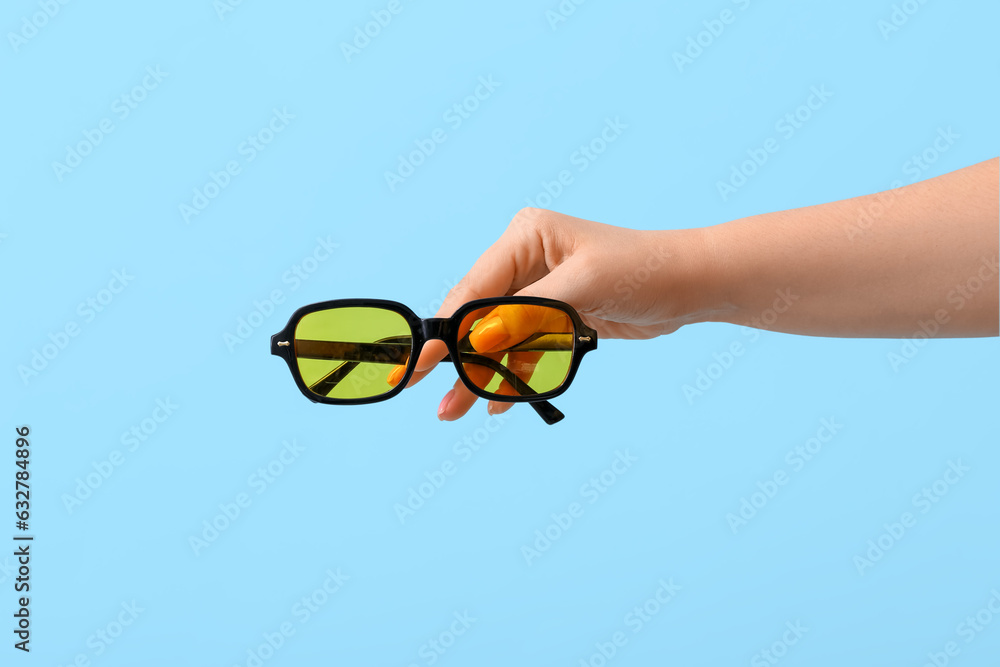 Woman holding stylish sunglasses on blue background