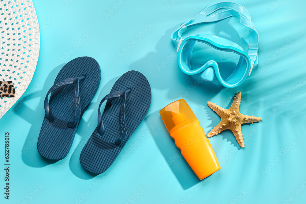 Female stylish flip flops with sunscreen cream and snorkeling mask on blue background